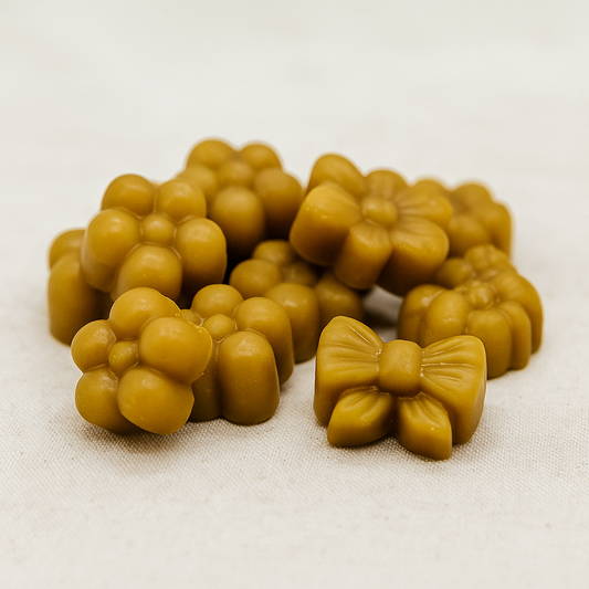 Fondants parfumés en cire d’abeille naturelle, en forme de fleurs et de nœuds, disposés sur un tissu en lin sur une table en bois, ambiance artisanale et chaleureuse sans emballage ni décor superflu.